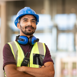 Male construction worker in hi-vis vest and blue hard hat wearing hearing protection showcasing AS/NZS 4602.1:2024 compliant safety gear in Australia.